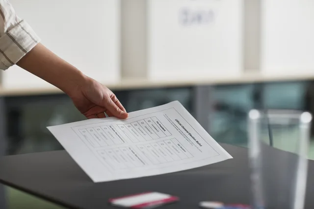 Close-up of a hand holding a ballot paper indoors, symbolizing democracy and civil rights. Survey routes for marketplace seller research